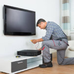Full length of male technician installing TV set top box at home